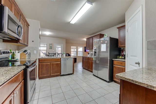 kitchen with appliances with stainless steel finishes, tasteful backsplash, sink, light tile patterned floors, and kitchen peninsula