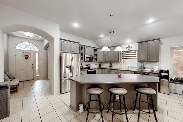 kitchen featuring a breakfast bar area, gray cabinetry, stainless steel appliances, tasteful backsplash, and a kitchen island