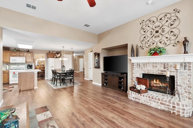 living room with a brick fireplace, ceiling fan with notable chandelier, and light hardwood / wood-style flooring