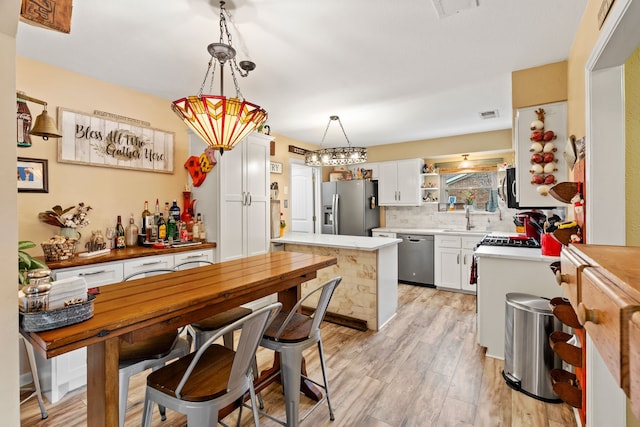 kitchen featuring sink, decorative light fixtures, light hardwood / wood-style flooring, appliances with stainless steel finishes, and white cabinets