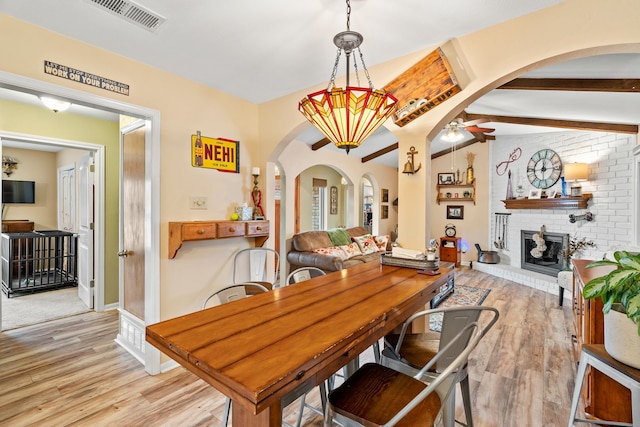 dining area with beam ceiling, a fireplace, light hardwood / wood-style floors, and ceiling fan