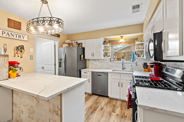 kitchen featuring appliances with stainless steel finishes, pendant lighting, white cabinetry, sink, and light hardwood / wood-style flooring