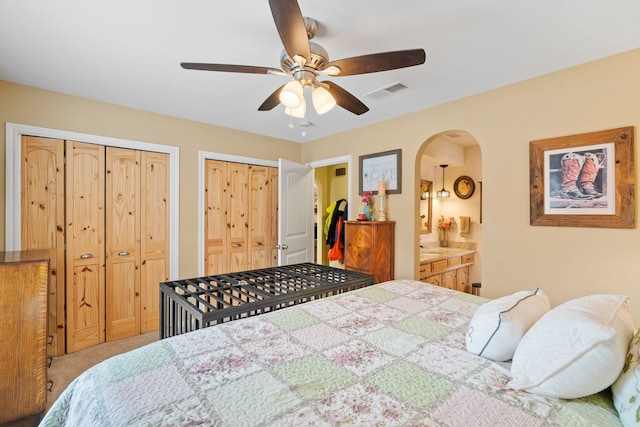 bedroom featuring connected bathroom, two closets, light colored carpet, and ceiling fan