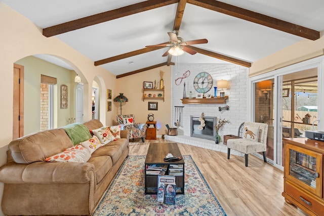 living room featuring ceiling fan, a fireplace, light hardwood / wood-style floors, and vaulted ceiling with beams