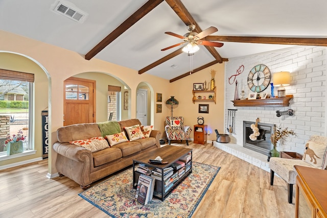 living room with ceiling fan, a fireplace, light wood-type flooring, and vaulted ceiling with beams