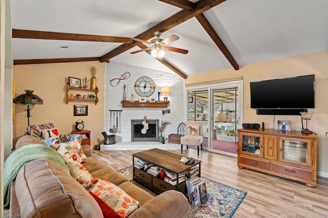 living room with ceiling fan, a fireplace, lofted ceiling with beams, and light wood-type flooring