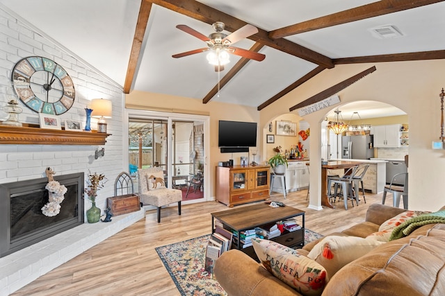 living room featuring vaulted ceiling with beams, a fireplace, light hardwood / wood-style floors, and ceiling fan