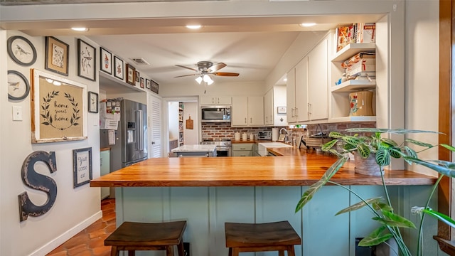 kitchen with wood counters, a breakfast bar, white cabinetry, appliances with stainless steel finishes, and kitchen peninsula