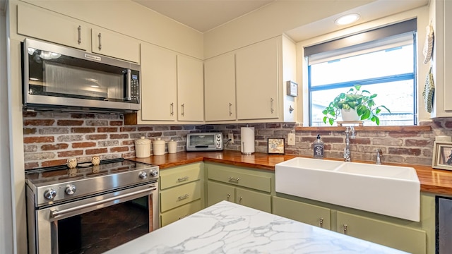 kitchen with butcher block countertops, sink, green cabinetry, and appliances with stainless steel finishes