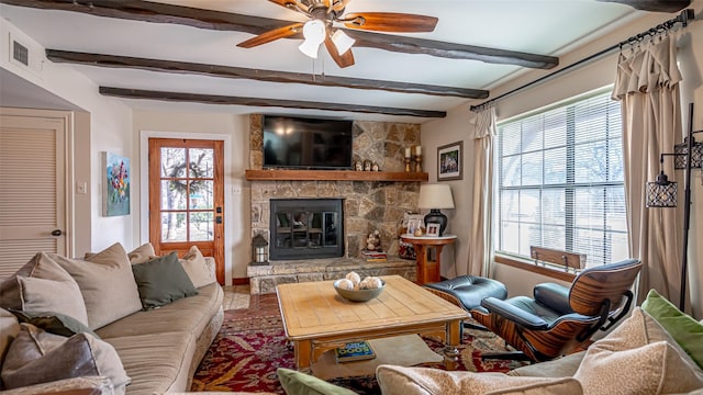 living room featuring ceiling fan, a stone fireplace, and beamed ceiling