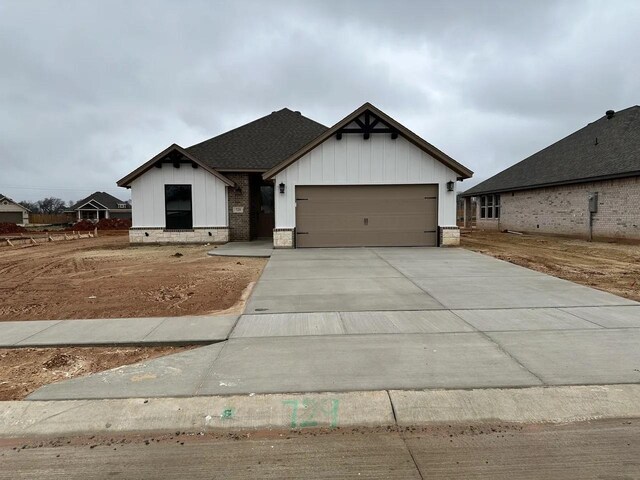 modern farmhouse style home with an attached garage, board and batten siding, driveway, and a shingled roof