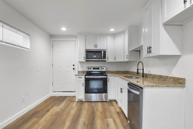 kitchen with appliances with stainless steel finishes, sink, white cabinets, light stone counters, and light hardwood / wood-style flooring