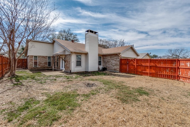 back of property with brick siding, a yard, a chimney, a patio, and a fenced backyard