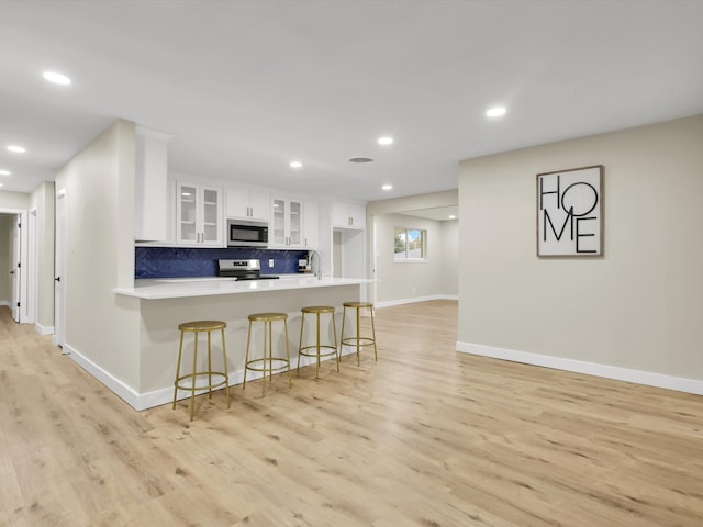 kitchen featuring appliances with stainless steel finishes, white cabinets, a kitchen bar, light hardwood / wood-style floors, and kitchen peninsula