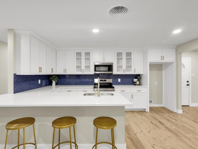 kitchen with stainless steel appliances, white cabinetry, light wood-type flooring, and a kitchen bar