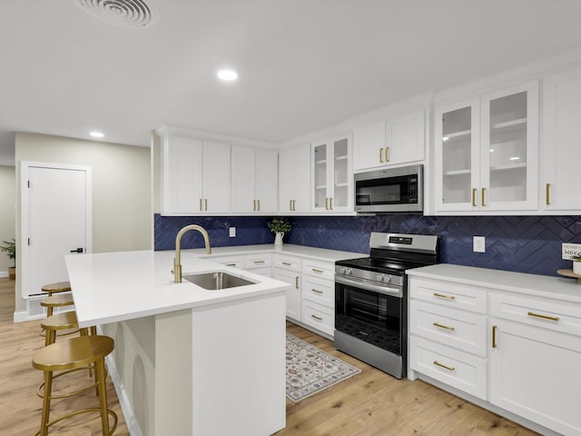 kitchen with an island with sink, sink, white cabinets, stainless steel appliances, and light wood-type flooring