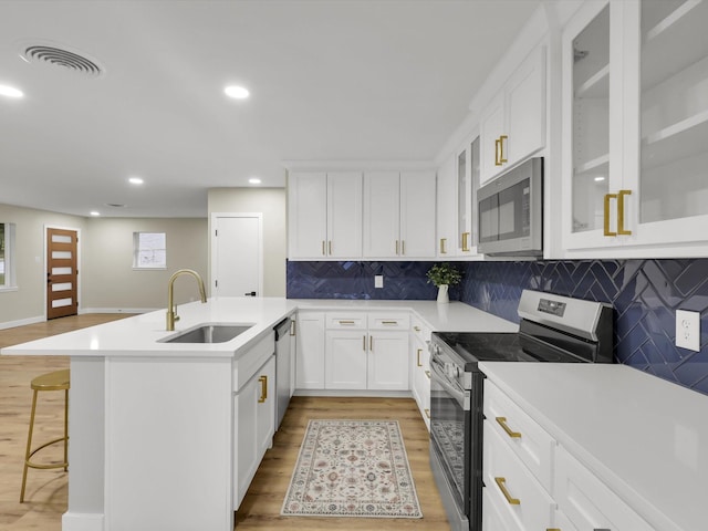 kitchen featuring appliances with stainless steel finishes, a breakfast bar, sink, white cabinets, and light wood-type flooring