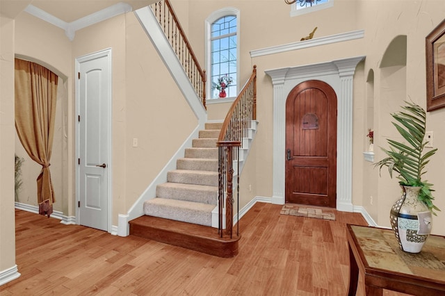 foyer entrance with a towering ceiling, ornamental molding, and light hardwood / wood-style floors