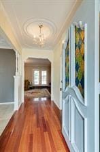 hall with an inviting chandelier, hardwood / wood-style floors, and ornamental molding