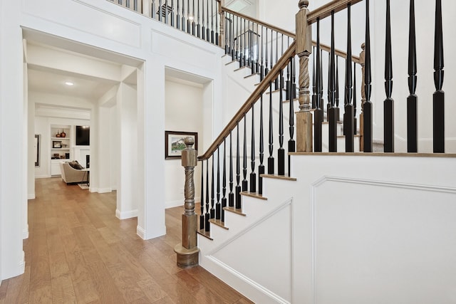 staircase with hardwood / wood-style floors, built in shelves, and a high ceiling