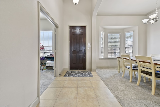 entryway with crown molding, light colored carpet, and a chandelier