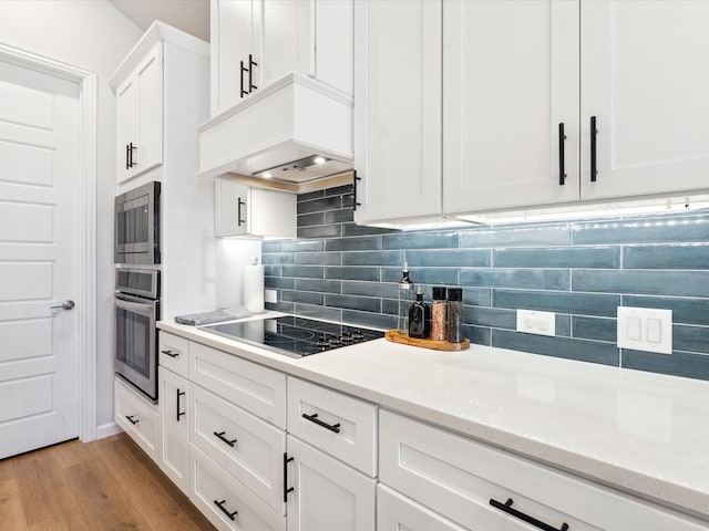 kitchen with premium range hood, black electric stovetop, white cabinets, decorative backsplash, and light wood-type flooring