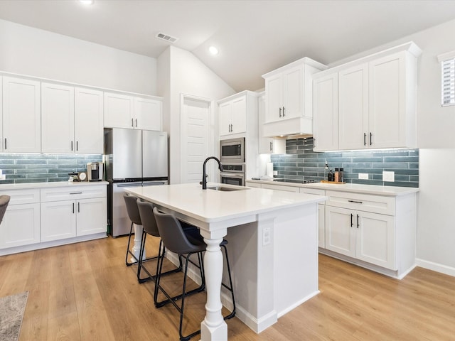 kitchen with sink, appliances with stainless steel finishes, a kitchen breakfast bar, an island with sink, and white cabinets