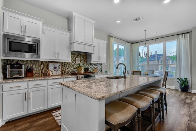 kitchen featuring stainless steel microwave, sink, white cabinetry, and a center island with sink