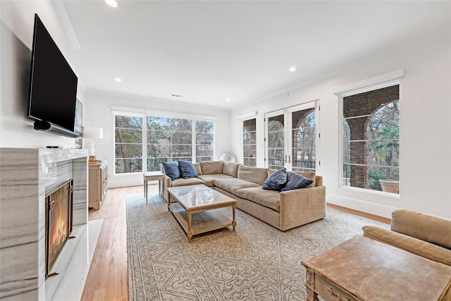 living room with a fireplace, french doors, crown molding, and light hardwood / wood-style flooring