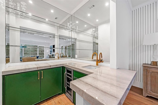 bar featuring green cabinetry, light hardwood / wood-style flooring, sink, ornamental molding, and beverage cooler