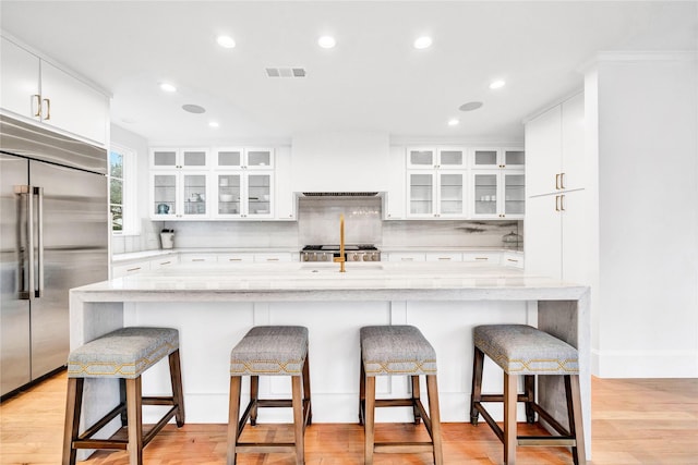 kitchen with built in fridge, premium range hood, light wood-type flooring, a kitchen breakfast bar, and white cabinets