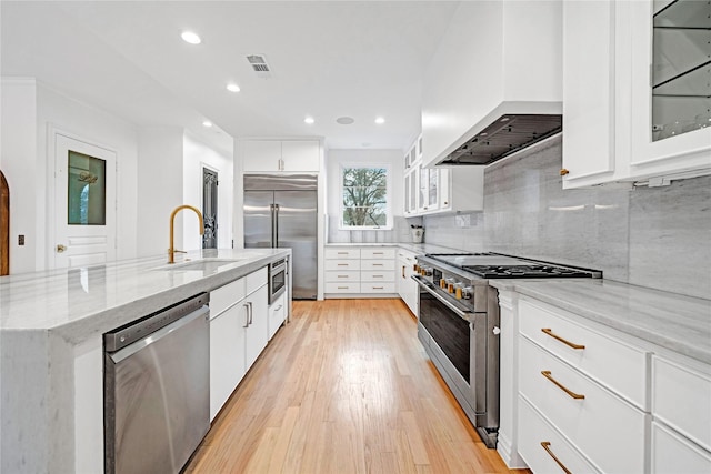 kitchen with white cabinetry, a center island with sink, built in appliances, sink, and custom exhaust hood