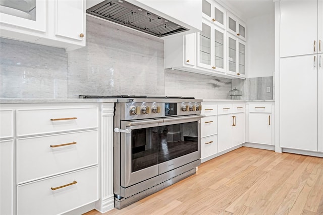 kitchen with light hardwood / wood-style floors, wall chimney exhaust hood, high end stove, white cabinets, and tasteful backsplash