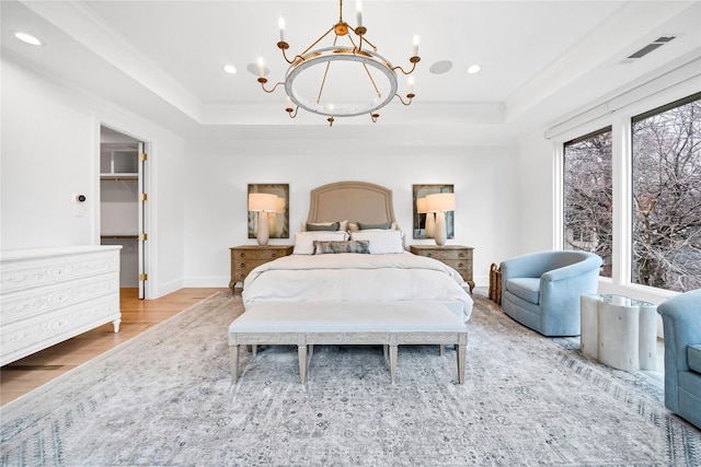 bedroom featuring an inviting chandelier, a walk in closet, a tray ceiling, light hardwood / wood-style floors, and crown molding