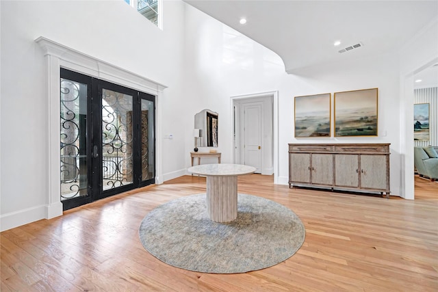 entrance foyer with light hardwood / wood-style floors, french doors, a healthy amount of sunlight, and a towering ceiling