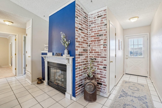 foyer entrance with light tile patterned floors, baseboards, a textured ceiling, and a glass covered fireplace