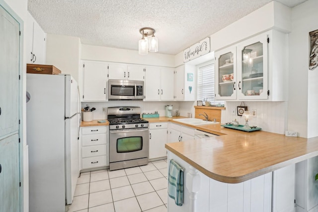 kitchen with light tile patterned floors, stainless steel appliances, a peninsula, a sink, and light countertops