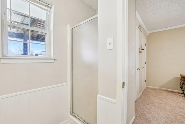 bathroom with a textured ceiling, ornamental molding, a stall shower, and wainscoting