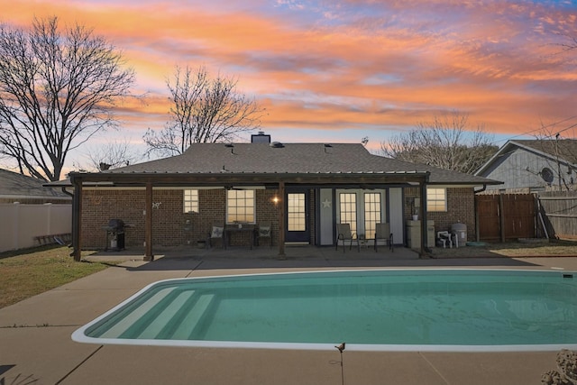 pool at dusk with a patio area, fence, and a fenced in pool