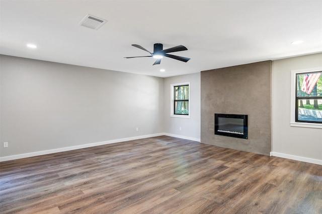 unfurnished living room featuring a large fireplace, dark hardwood / wood-style floors, and ceiling fan