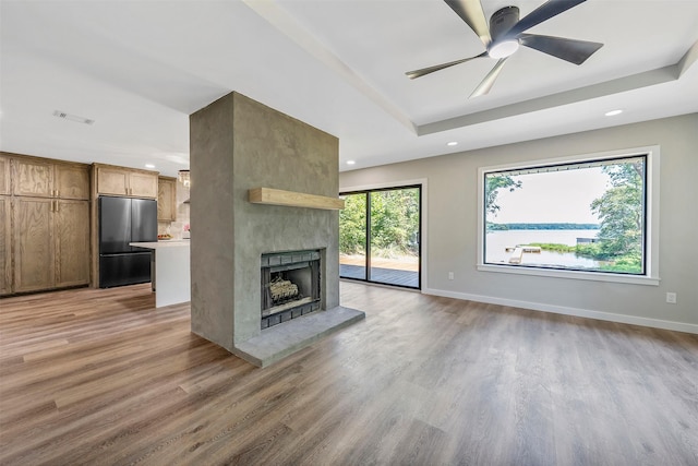 unfurnished living room featuring a fireplace, a tray ceiling, wood-type flooring, and ceiling fan