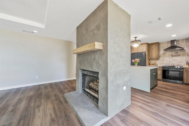 kitchen with stainless steel stove, fridge, a large fireplace, dark hardwood / wood-style flooring, and wall chimney exhaust hood