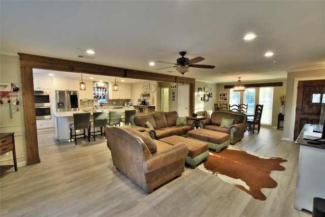 living room with crown molding, ceiling fan with notable chandelier, and light wood-type flooring