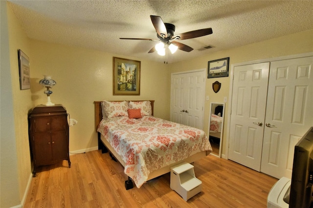 bedroom with multiple closets, light hardwood / wood-style flooring, a textured ceiling, and ceiling fan