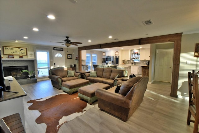 living room with a brick fireplace, crown molding, and light wood-type flooring