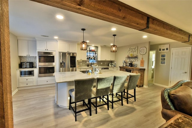 kitchen with pendant lighting, appliances with stainless steel finishes, light stone counters, an island with sink, and white cabinets