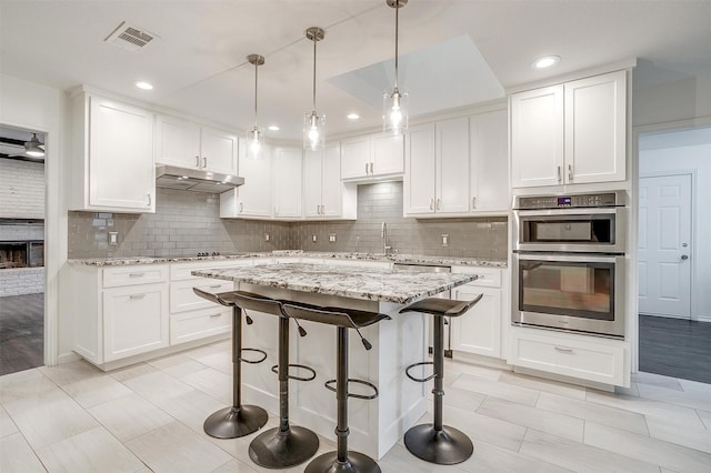 kitchen with pendant lighting, light stone counters, stainless steel double oven, and white cabinets