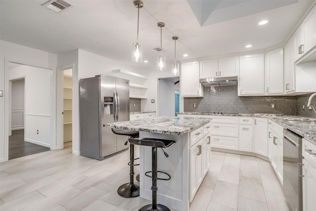 kitchen with decorative light fixtures, a center island, white cabinets, and appliances with stainless steel finishes