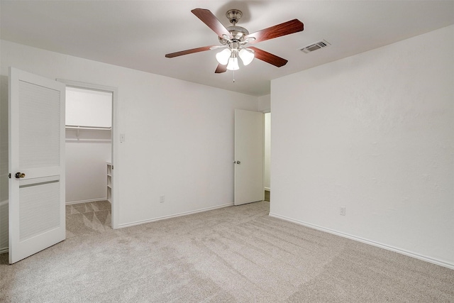 unfurnished bedroom featuring light carpet, a walk in closet, a closet, and ceiling fan