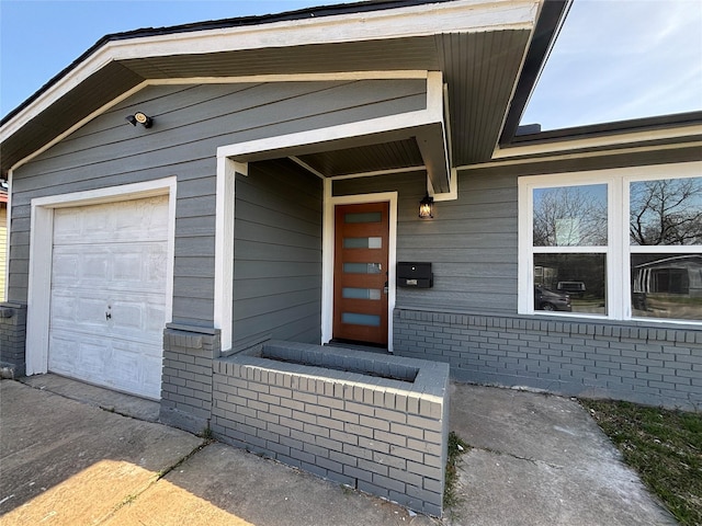 view of exterior entry featuring a garage and brick siding